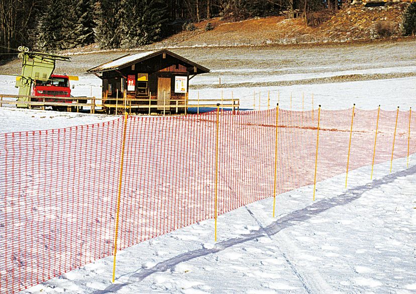 Schneefangzaun, orange, im Schnee mit kleinem Haus im Hintergrund, Bild im Freien